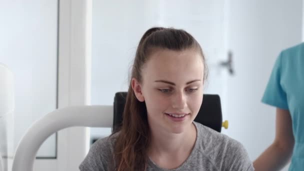 Jonge vrouw doet oefeningen op simulator met therapeut in de sportschool — Stockvideo