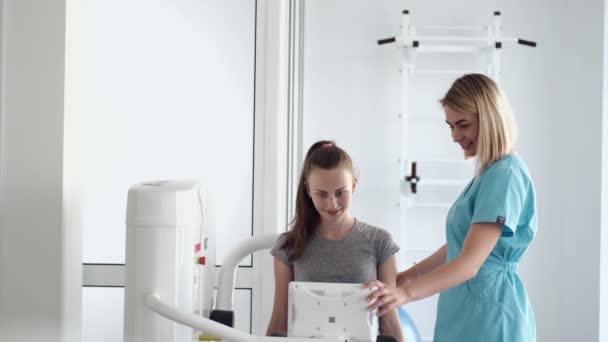 Jonge vrouw doet oefeningen op simulator met therapeut in de sportschool — Stockvideo