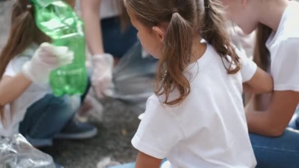 Маленькая девочка в белой футболке собирает мусор в лесу — стоковое видео