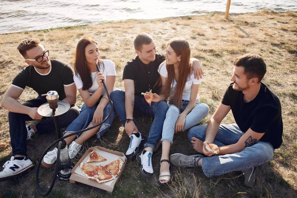 Young people eating pizza smoking shisha outside