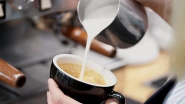 The barista is pouring milk into a mug of espresso