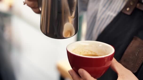 The barista is pouring milk into a mug of espresso — Stok video