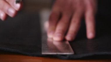 The tanner is cutting black leather sheet with a razor and metre