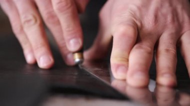 The tanner is cutting black leather sheet with a razor and metre