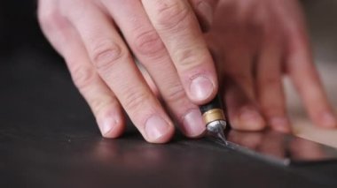 The tanner is cutting black leather sheet with a razor and metre