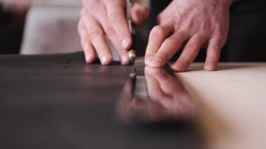 The tanner is cutting black leather sheet with a razor and metre