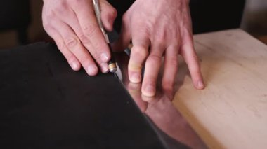 The tanner is cutting black leather sheet with a razor and metre