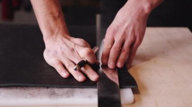 The tanner is cutting black leather sheet with a razor and metre