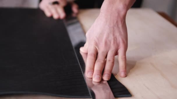 El curtidor está cortando la hoja de cuero negro con una cuchilla y un metro — Vídeos de Stock