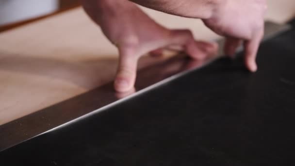 El curtidor está cortando la hoja de cuero negro con una cuchilla y un metro — Vídeo de stock