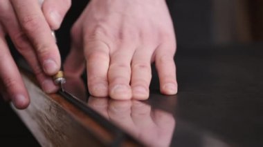 The tanner is cutting black leather sheet with a razor and metre