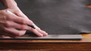 The tanner is cutting black leather sheet with a razor and metre