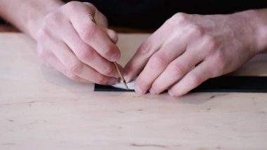 The leather craftsman is marking the end of a belt tail