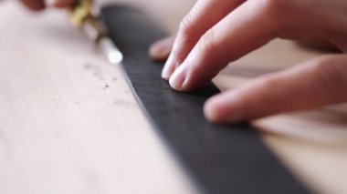 The leather craftsman is cutting the edges of a belt