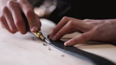 The leather craftsman is cutting the edges of a belt