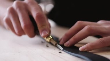 The leather craftsman is cutting the edges of a belt