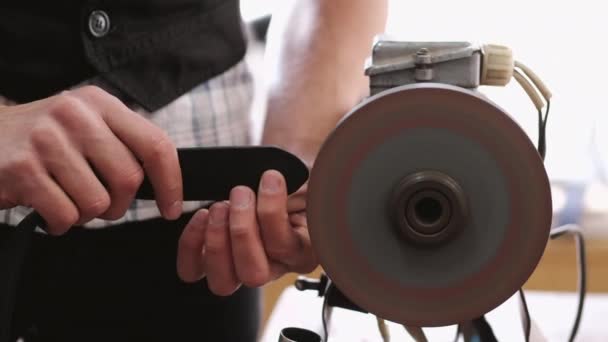 El artesano está afilando los bordes de un cinturón en una máquina especial — Vídeo de stock