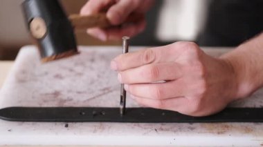 The leather craftsman is making holes in a hand-made belt