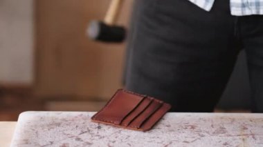 The tanner is stitching a hand-made leather wallet