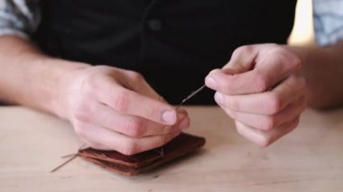 The tanner is stitching a hand-made leather wallet