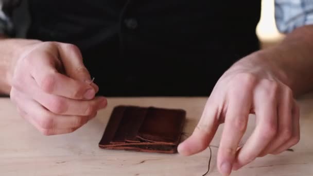 The tanner is stitching a hand-made leather wallet — ストック動画