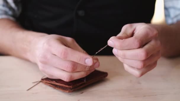 The tanner is stitching a hand-made leather wallet — Stock video