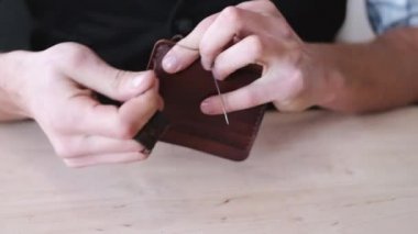 The tanner is stitching a hand-made leather wallet