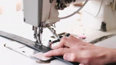 The craftsman stitches a mens leather belt on a sewing machine