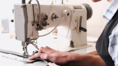 The craftsman stitches a mens leather belt on a sewing machine