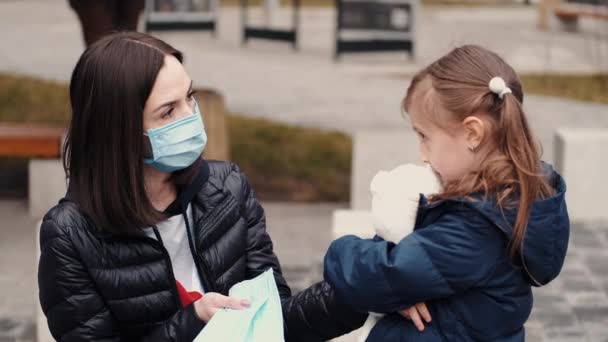 Žena v masce na jedno použití učí své dítě nosit respirátor — Stock video