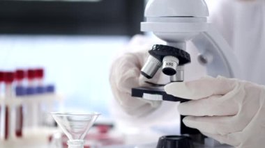 Scientist in a coverall suit is adjusting a microscope in a modern lab