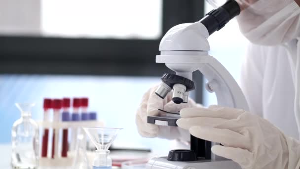 Scientist in a coverall suit is adjusting a microscope in a modern lab — 图库视频影像