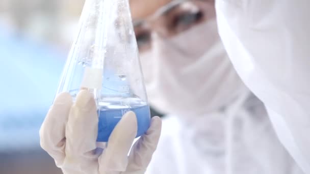 Uno scienziato di laboratorio sta esaminando una soluzione blu in una bottiglia — Video Stock