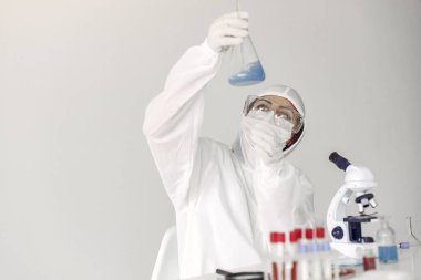 Bir laboratuvar bilimcisi mavi çözeltiyi şişede inceliyor.
