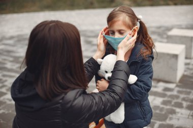 Tek kullanımlık maskeli bir kadın çocuğuna solunum cihazı takmayı öğretiyor.