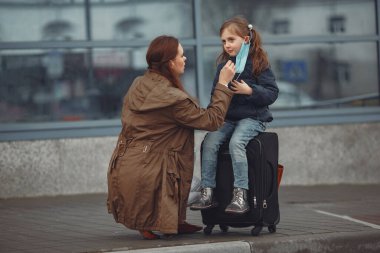 Kızıyla birlikte solunum cihazına bağlı Avrupalı bir anne binanın yanında duruyor. Ebeveyn kendini virüsten korumak için çocuğuna koruyucu maske takmayı öğretiyor.