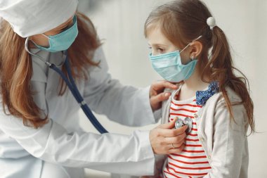 Doktor bir kadın steteskoplu bir çocuğu muayene ediyor.