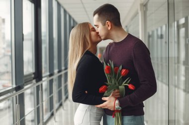 Avrupalı çift bir grup kırmızı laleyle bir salonda duruyor.