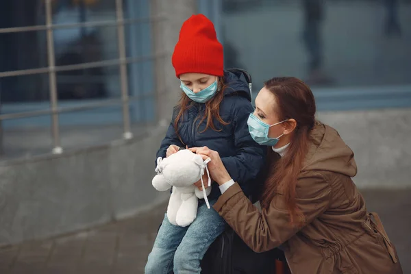 Una madre europea en un respirador con su hija está de pie cerca de un edificio.El padre le está enseñando a su hijo a usar máscara protectora para salvarse del virus. —  Fotos de Stock