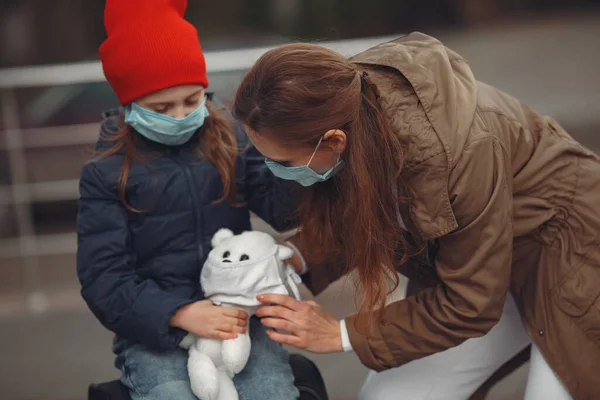 Una madre europea en un respirador con su hija está de pie cerca de un edificio.El padre le está enseñando a su hijo a usar máscara protectora para salvarse del virus. — Foto de Stock