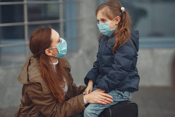 Una madre europea en un respirador con su hija está de pie cerca de un edificio.El padre le está enseñando a su hijo a usar máscara protectora para salvarse del virus. — Foto de Stock
