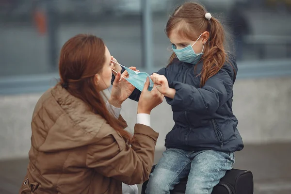 Una madre europea en un respirador con su hija está de pie cerca de un edificio.El padre le está enseñando a su hijo a usar máscara protectora para salvarse del virus. — Foto de Stock