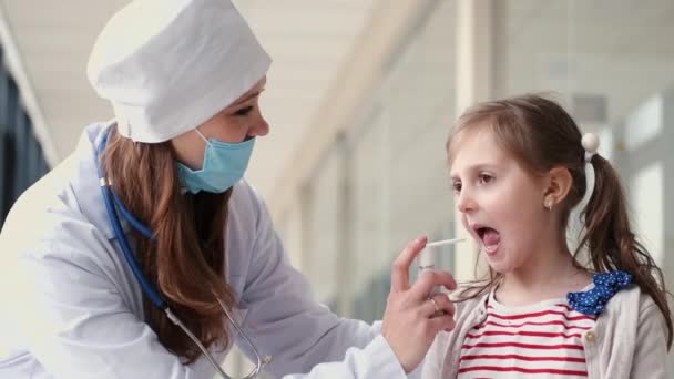 The doctor in a mask is sparing throat antiseptic for a child — Stock Video