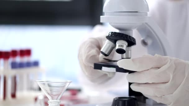 Scientist in a coverall suit is adjusting a microscope in a modern lab — Wideo stockowe