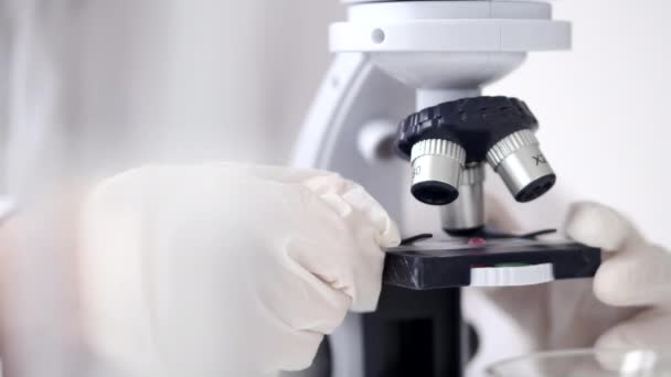 Ilmuwan dalam setelan terselubung sedang menyesuaikan mikroskop di laboratorium modern — Stok Video
