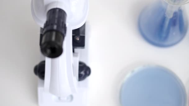 Microscopio y soluciones azules están en una mesa de laboratorio — Vídeo de stock