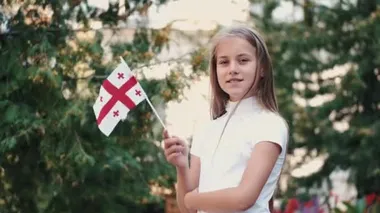 Elinde Gürcü bayrağı tutan küçük kız dışarıda duruyor.