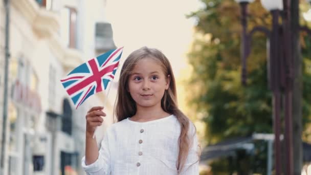Chica rubia sosteniendo bandera británica afuera en la calle — Vídeo de stock