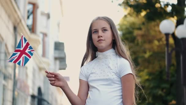 Menina loira segurando bandeira britânica fora na rua — Vídeo de Stock