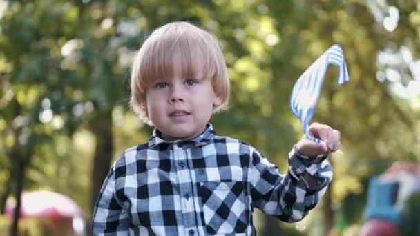 Портрет мальчика, играющего с греческим флагом в парке — стоковое видео